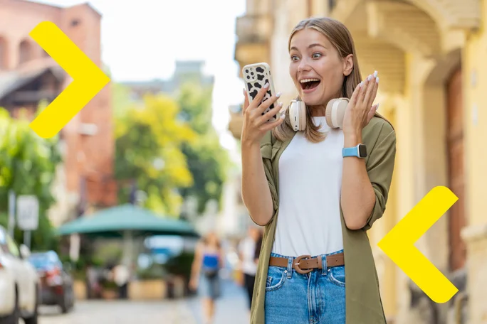 young girl holding her phone in the street and being surprised while looking at her phone