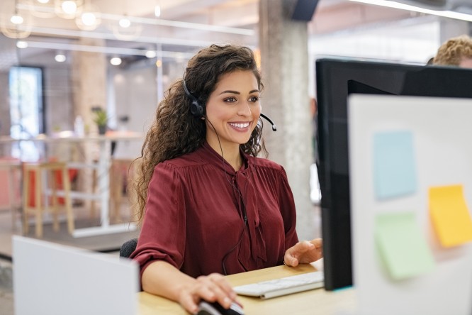 Customer support phone operator working at computer. Happy call center agent working on support hotline in office. Smiling call center agent in conversation with customer over headset.